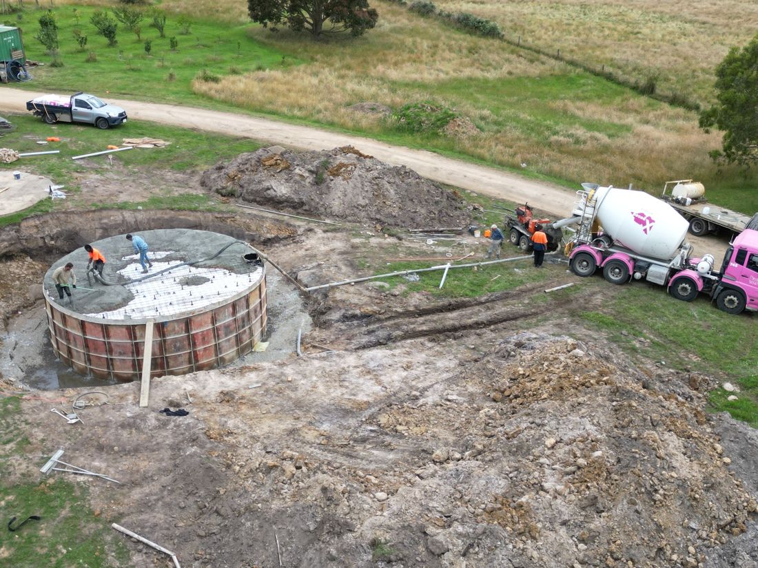Workers pouring concrete into circular foundation with cement mixer truck at rural construction site.